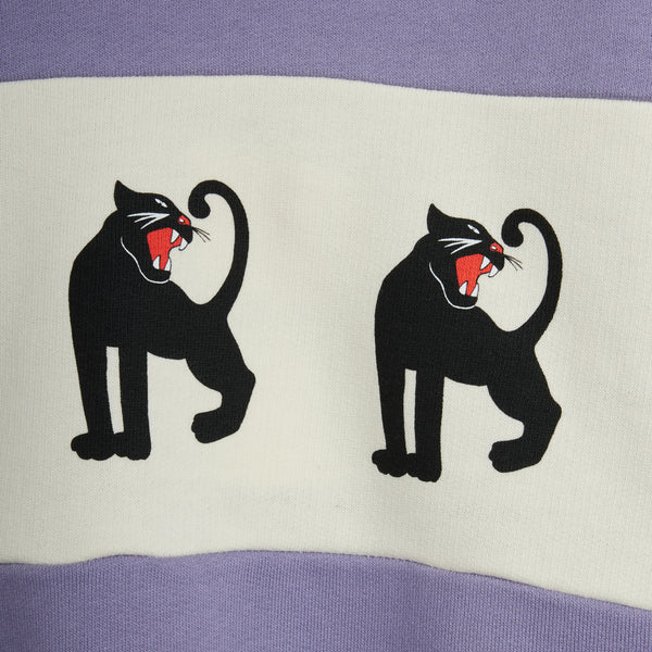Close-up of a sweatshirt featuring a lavender purple top and bottom band with a wide white center panel. The center panel displays two black panther silhouettes facing each other, with their red tongues sticking out.