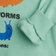 Close-up of a mint green sweatshirt featuring a graphic print of a blue worm and an orange worm tail, with a ribbed cuff showing a soft fleece lining.