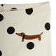 Close-up of cream ribbed fabric with large black polka dots and an embroidered brown dachshund on the front.