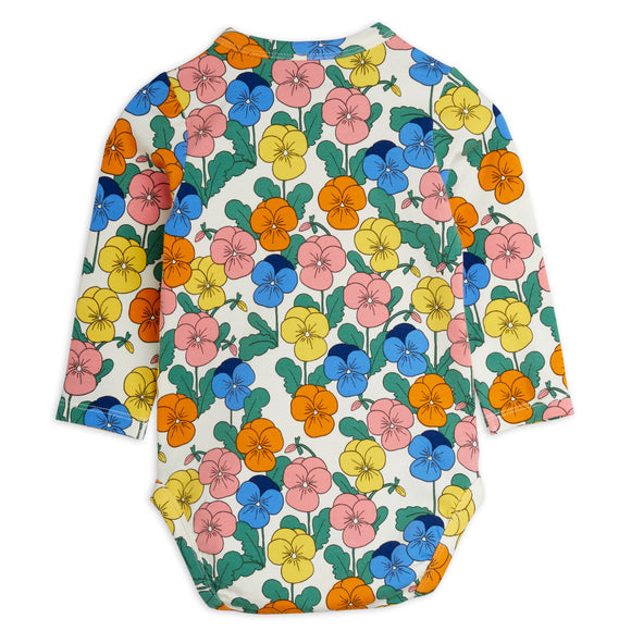 A long-sleeve baby bodysuit featuring a colorful floral print of pansies in pink, blue, yellow, and orange on an off-white background, shown flat against a white studio backdrop.
