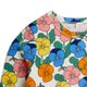 A close-up of a children's long-sleeve top featuring a colorful pansy floral print on an off-white background. The print includes pink, blue, yellow, and orange flowers with green leaves.