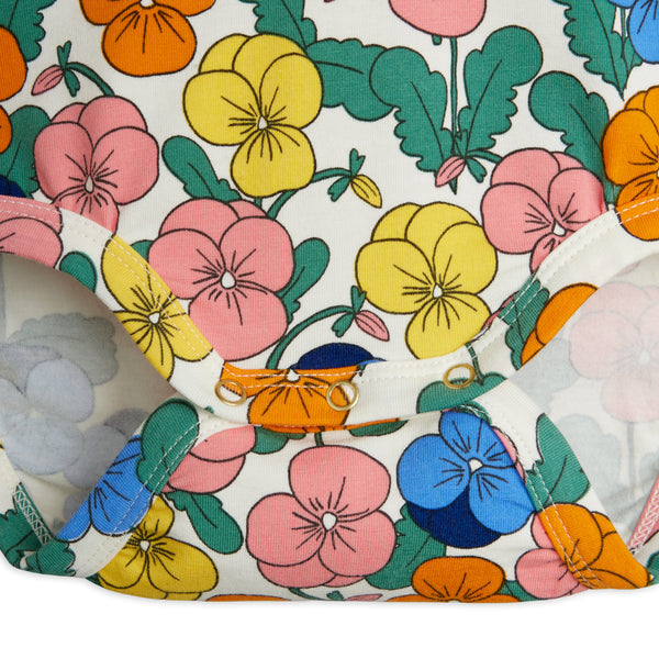 A close-up of a floral-patterned fabric item, likely a diaper cover or baby bootie, featuring a retro pansy print in pink, yellow, blue, and orange on a cream background.