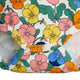 A close-up of a floral-patterned fabric item, likely a diaper cover or baby bootie, featuring a retro pansy print in pink, yellow, blue, and orange on a cream background.