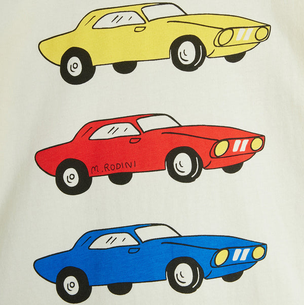 A close-up of a white fabric surface printed with three cartoon-style muscle cars stacked vertically: a yellow car at the top, a red car in the middle with 'M. RODINI' text on the side, and a blue car at the bottom.