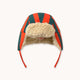 A chapka hat featuring the brand's signature red and green striped wool fabric, a beige sherpa fleece lining, and red ear loops, shown against a plain off-white background.