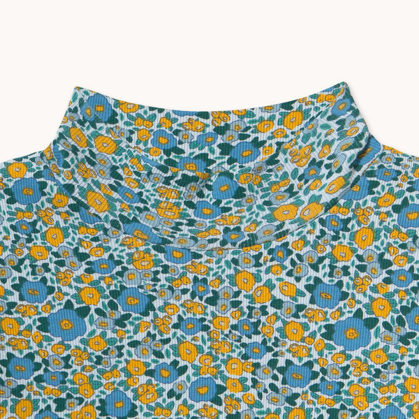 Close-up of a floral-patterned top with a high mock neck, featuring yellow and blue flowers on a teal and white background.