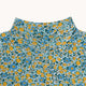 Close-up of a floral-patterned top with a high mock neck, featuring yellow and blue flowers on a teal and white background.