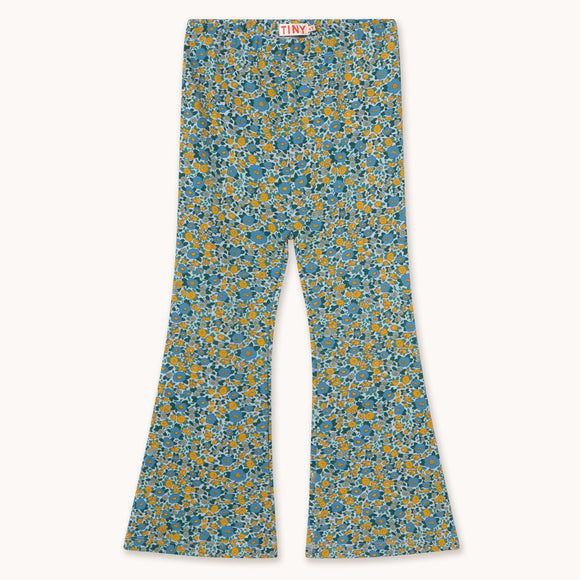 A pair of wide-leg pants featuring a dense blue and yellow floral pattern on a light teal base, laid flat against a light cream background.