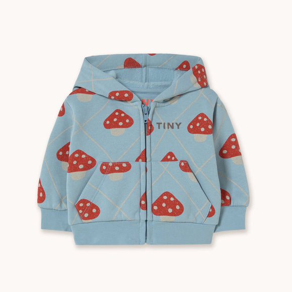 A light blue zip-up hoodie for kids, featuring an all-over print of red and white mushrooms, with the brand name 'TINY' printed on the chest, displayed against a solid off-white background.