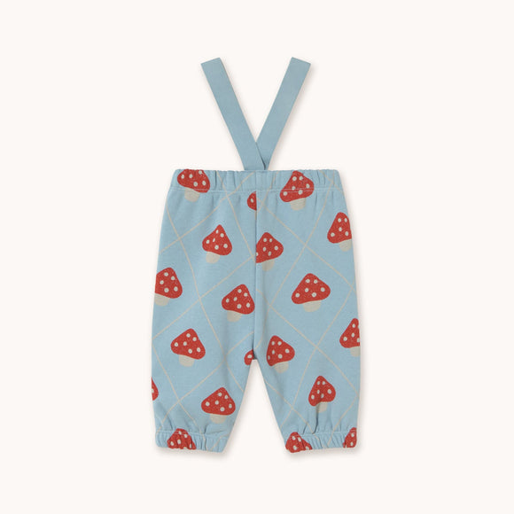 Light blue baby pants with red and white mushroom print and adjustable shoulder straps, shown flat on a light beige background.