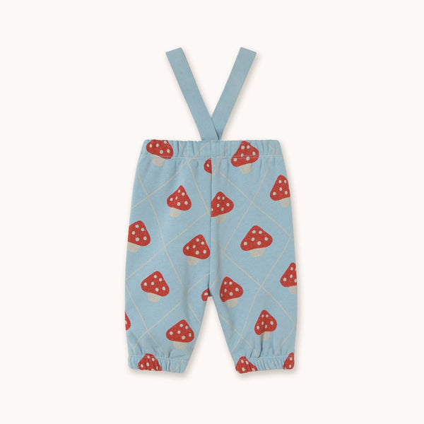Light blue baby pants with red and white mushroom print and adjustable shoulder straps, shown flat on a light beige background.