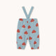 Light blue baby pants with red and white mushroom print and adjustable shoulder straps, shown flat on a light beige background.