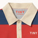 Close-up of a striped polo shirt collar and button placket with navy, red, and cream horizontal stripes. The inside collar shows the brand name 'TINY' in red, and 'TINY' is printed in white on the chest.