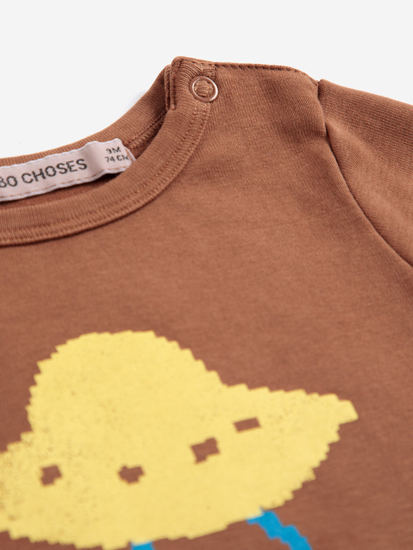 Close-up of a brown children's long-sleeve top with a yellow pixelated cloud graphic and a visible neck label reading 'CHOSES'.