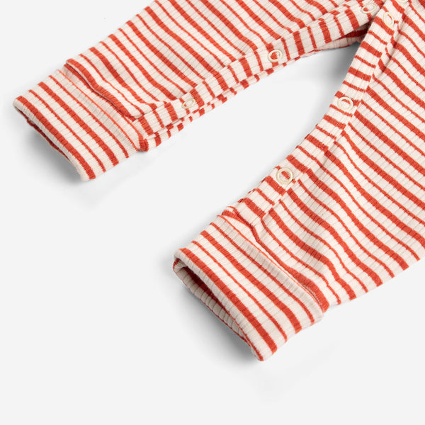 Close-up of a striped garment, likely a baby romper or pants, featuring alternating red-orange and cream horizontal stripes with a buttoned cuffed sleeve.