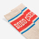 A close-up of a ribbed knit sock in cream with a bold red band, blue stripes, and white 'BOBO CSES' lettering, photographed on a light gray background.