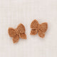 A pair of small crocheted butterfly-shaped hair clips in a warm camel brown color, displayed on a textured off-white linen background.