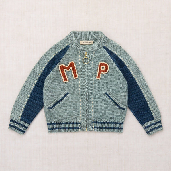 A light blue knit zip-up cardigan with navy blue raglan sleeves and ribbed trim, featuring large red embroidered letters 'M' and 'P' on the chest, laid flat on a light textured background.