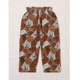 A pair of children's elastic-waist pants with an abstract geometric print in terracotta, brown, beige, and navy blue, laid flat on a textured beige fabric background.