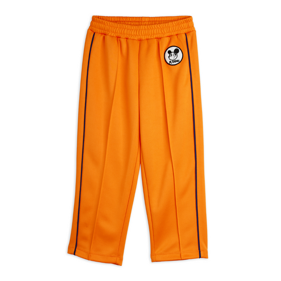 Bright orange athletic pants with black side stripes and a circular black-and-white logo patch on the upper left leg, shown flat against a white background.