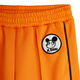 Close-up of bright orange athletic shorts with an elastic waistband, a circular black-and-white embroidered patch featuring a cartoon face and the text 'M.RODINI', and a thin dark blue side stripe.