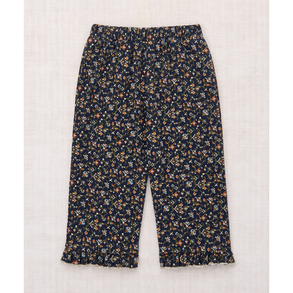 A pair of cropped pants with an all-over small floral print on a dark navy background, laid flat on a light beige textured fabric background.