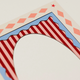 A close-up of a paper arch template or craft cutout with red and white stripes, a blue scalloped border, and a beige diamond pattern with a red star on a light background.