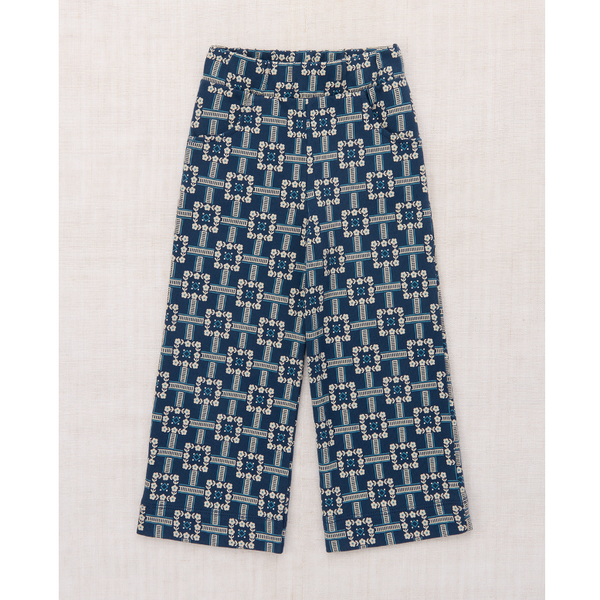 A pair of cropped pants with an elastic waistband, featuring a repeating geometric pattern in navy blue, light blue, and white, laid flat on a textured off-white background.
