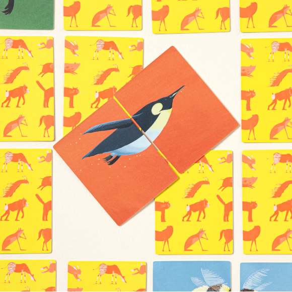 A close-up of a card game or deck layout featuring illustrated cards. A central orange card shows a penguin, surrounded by yellow cards with orange horse motifs and other partially visible cards in green and blue.