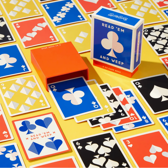 A deck of playing cards labeled 'READ 'EM AND WEEP' with an orange card box and blue/orange card box standing on a yellow surface surrounded by scattered cards in blue, red, black, and white.