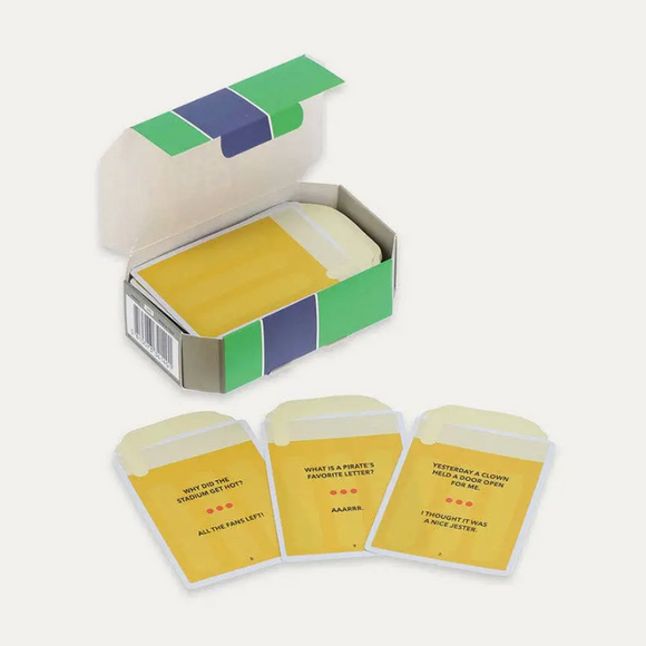 A boxed card game set with an open box containing pale yellow cards and three matching cards displayed in front on a light warm gray background.