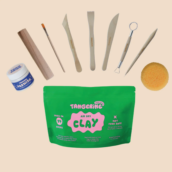 Tangerine Clay air-dry kit featuring a green resealable pouch, a small jar of watercolor paint, and seven sculpting tools arranged on a light beige background.