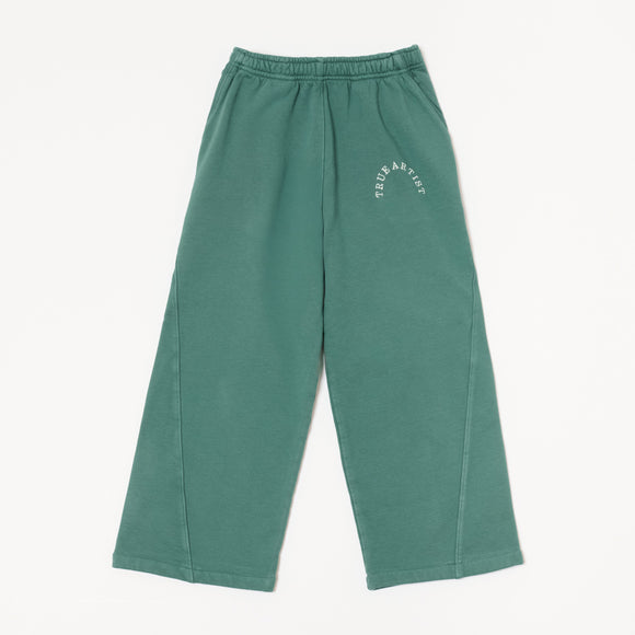 A pair of green sweatpants with a white curved 'TRUE ARTIST' logo printed on the upper left thigh, displayed flat against a light off-white background.