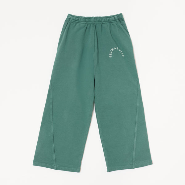 A pair of green sweatpants with a white curved 'TRUE ARTIST' logo printed on the upper left thigh, displayed flat against a light off-white background.