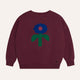 Maroon sweatshirt with a colorful flower design on a beige background