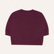 A dark plum purple cropped sweatshirt with long sleeves and ribbed cuffs, shown from the back on a light cream background.